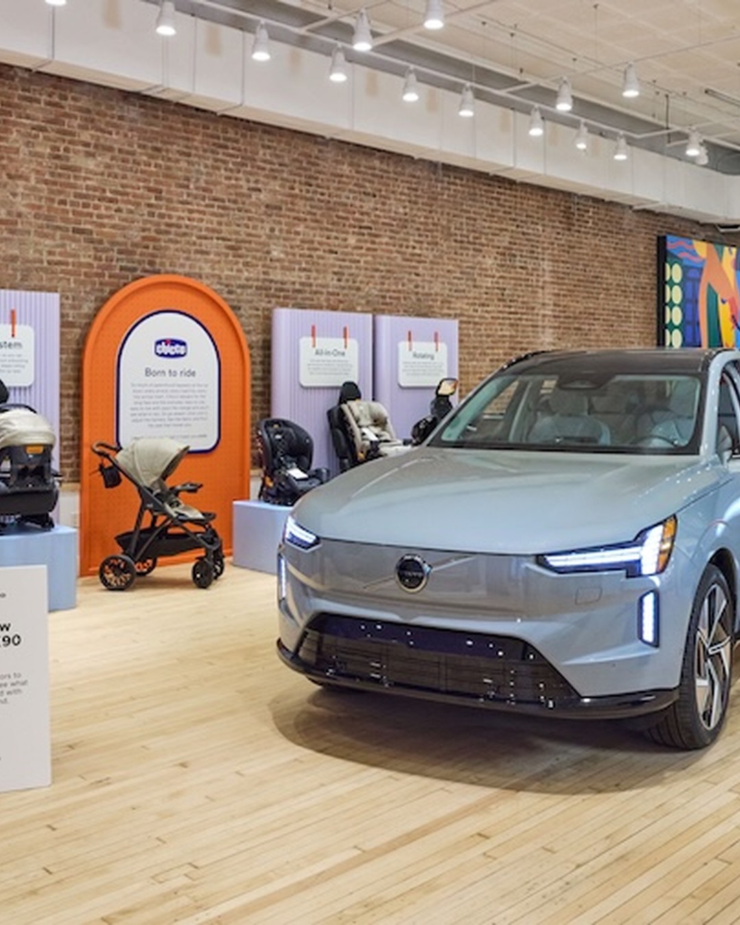 A wall of infant and convertible car seats on lilac plinths beside a full-size Volvo EX90 parked inside the showroom.