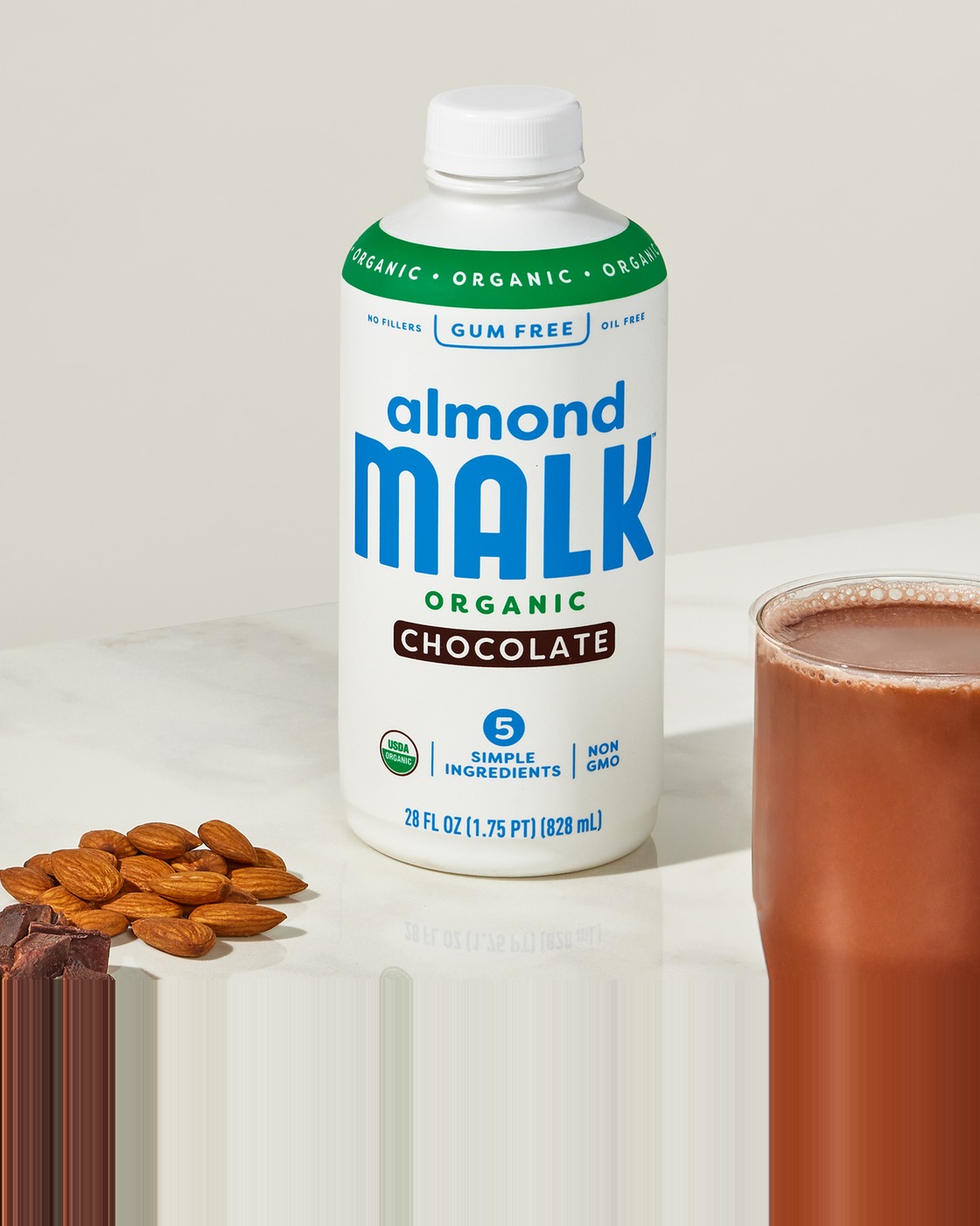 A bottle of MALK Chocolate Almond Milk beside a glass of chocolate milk and a scatter of almonds.