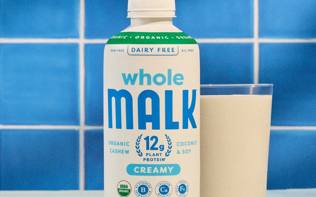 A bottle of Whole MALK plant-based milk beside a full glass on a blue tiled counter.