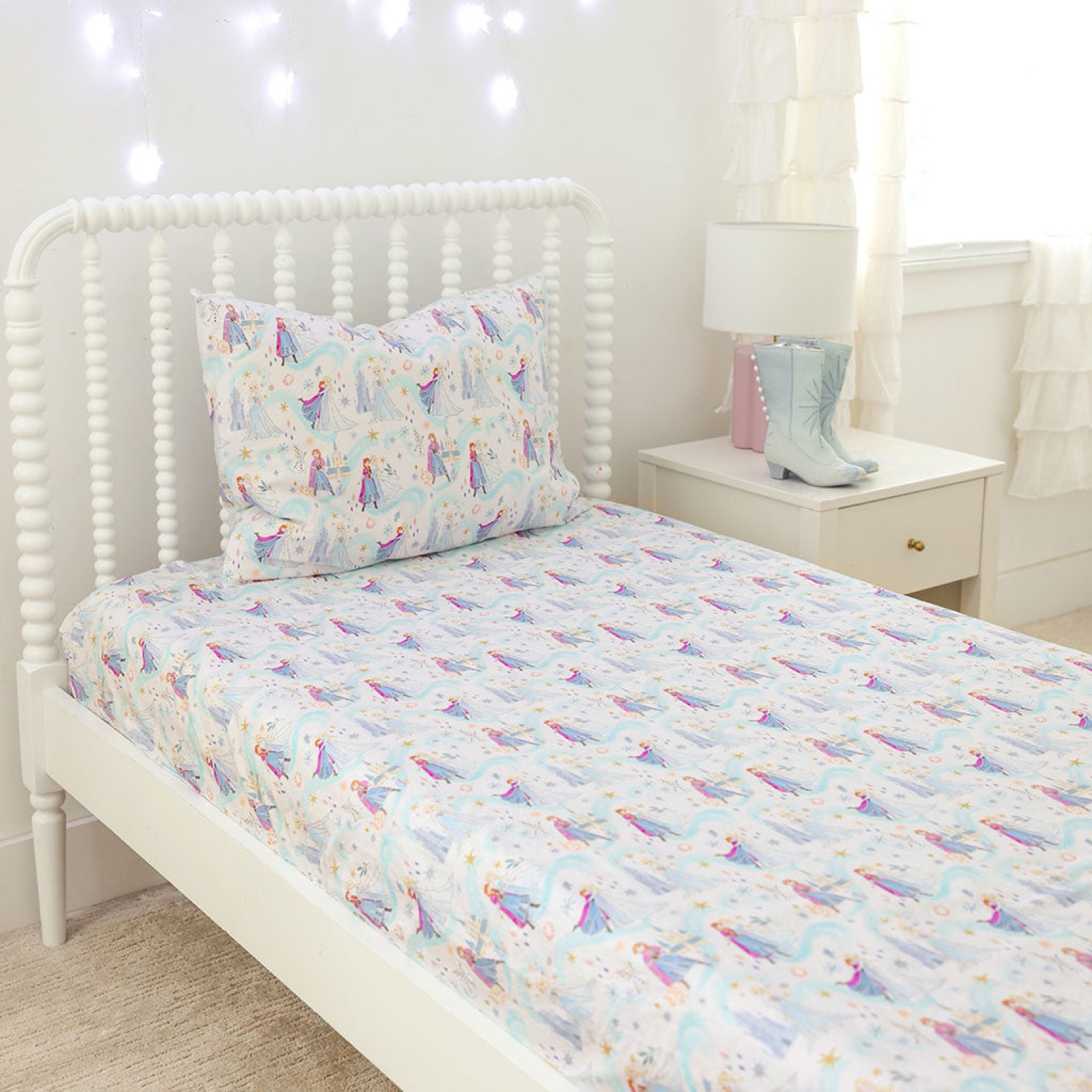 A white spindle bed made up with Posh Peanut's Elsa and Anna sheet set, pale blue with the Frozen sisters and snowflakes printed across it.