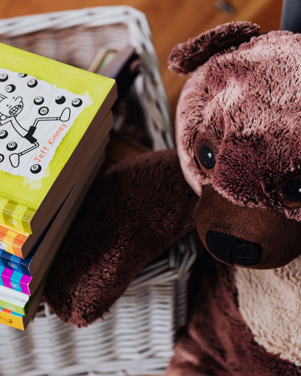 A stack of picture books in a basket beside a teddy bear.