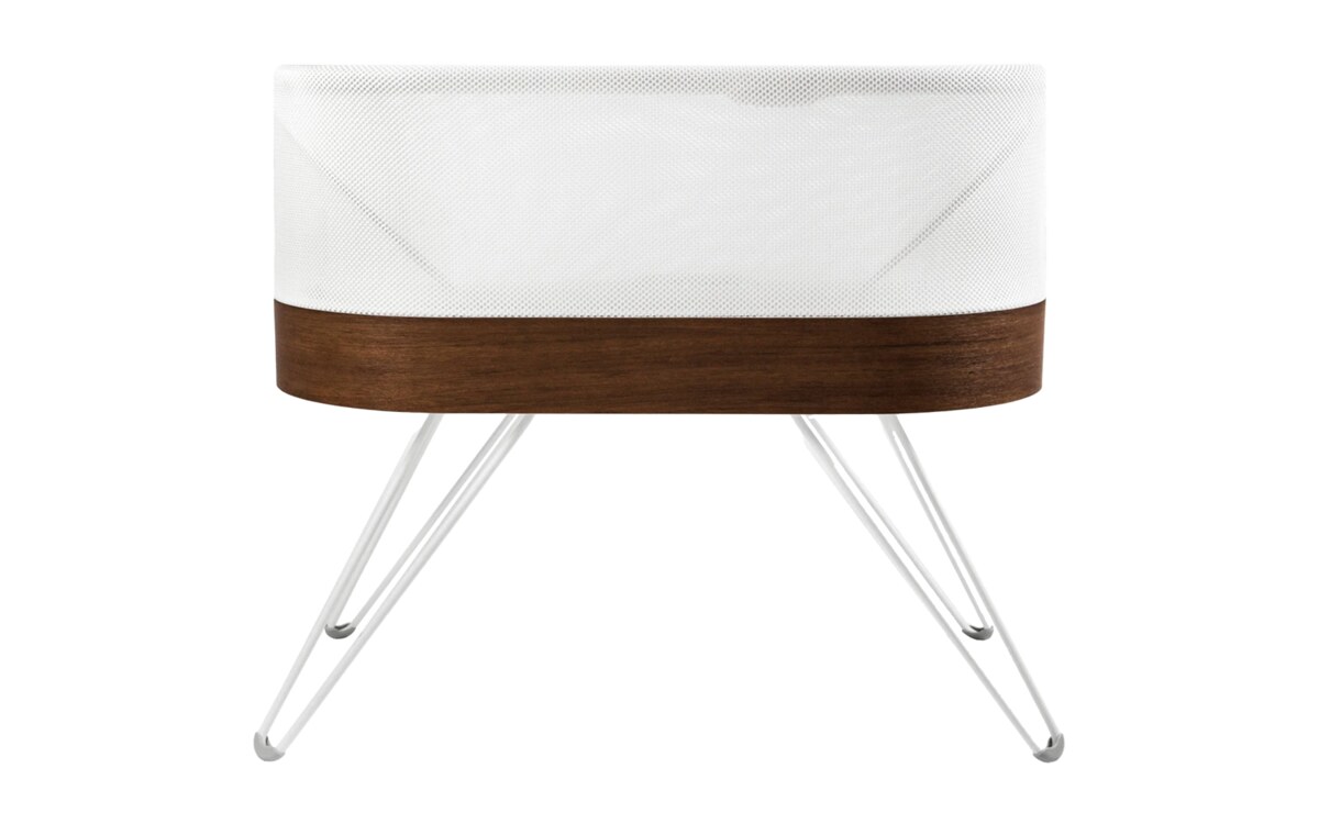 The SNOO Smart Sleeper bassinet, white mesh with a walnut band and white legs, on a white background.