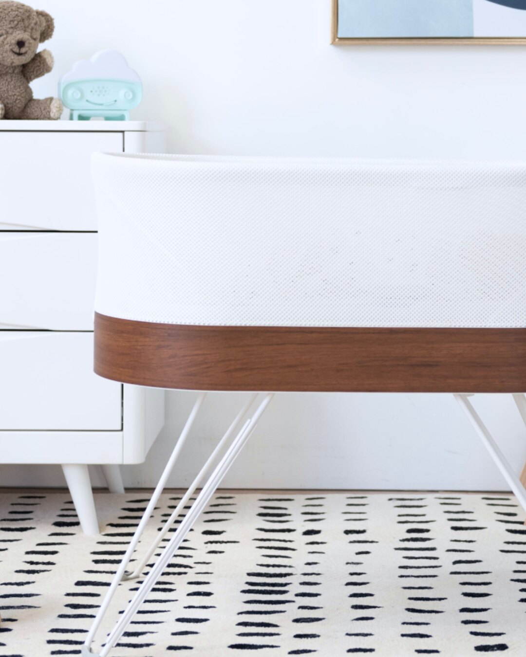 The SNOO Smart Sleeper bassinet standing beside a white dresser in a nursery, with no people in frame.